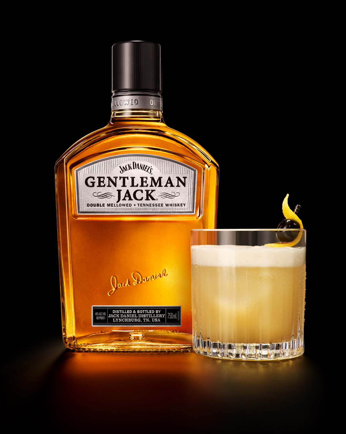 Botella Gentleman Jack junto a un cóctel con espuma, cereza y twist de limón